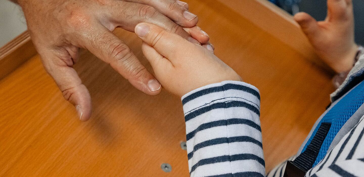 Betreuer hält die Hand eines Kindes